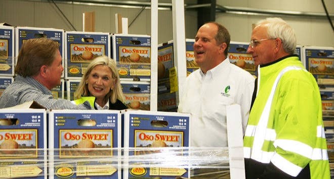 Team members talking on a warehouse floor stacked with boxes of imported sweet onions